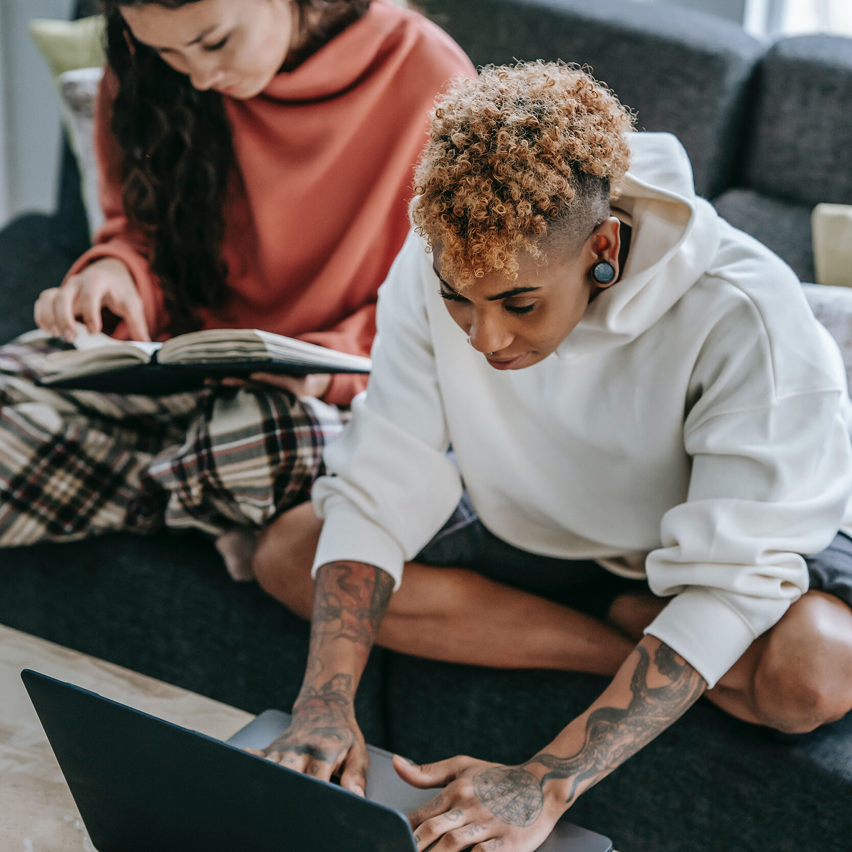 two young people sitting on a couch in their pajamas doing research on a laptop